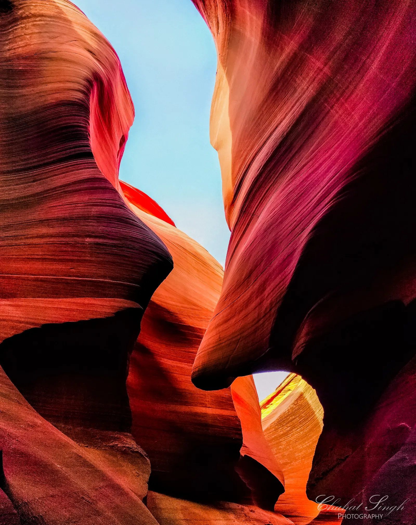 A narrow slot of blue sky visible between towering magenta and orange sandstone canyon walls.
