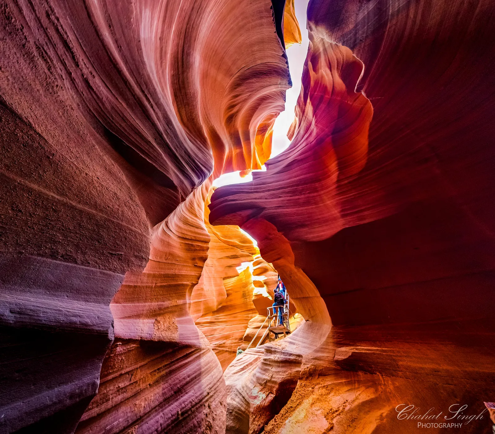 A visitor descending a metal stairway deep inside the glowing swirled walls of Antelope Canyon.