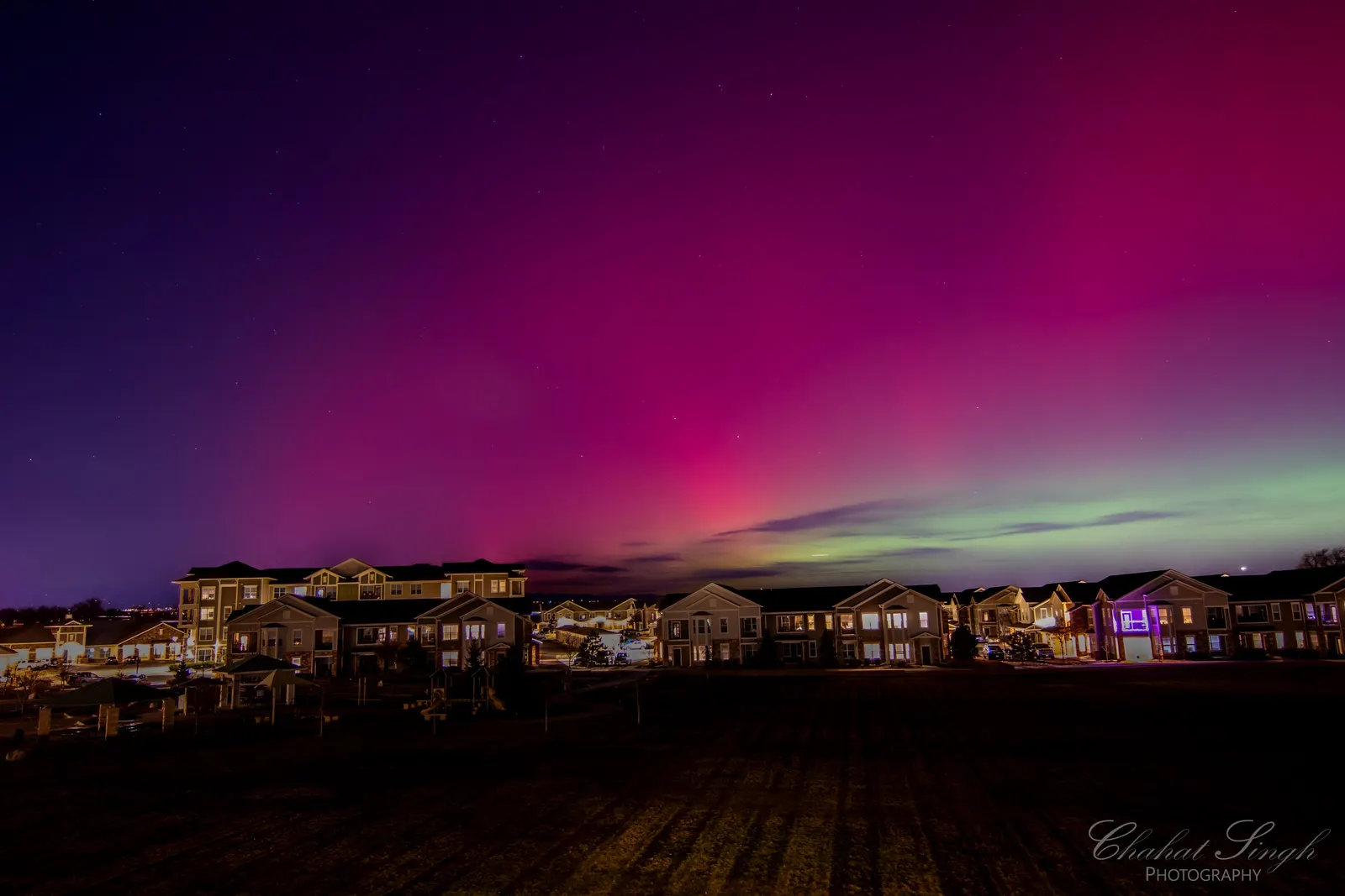 Purple and green aurora borealis lighting up the night sky above a suburban neighborhood.