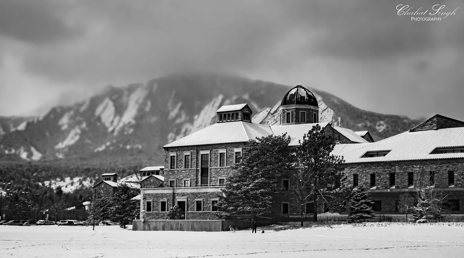 A stone building dusted with snow beneath the Flatirons mountains, in black and white.