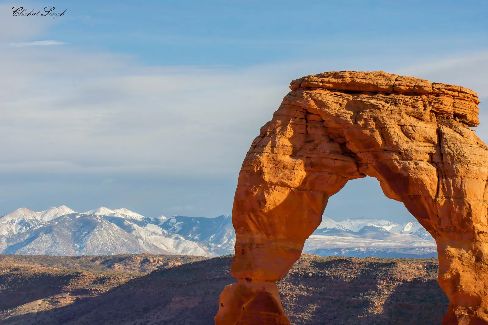 Delicate Arch framed against the snow-covered La Sal Mountains under a pale sky.