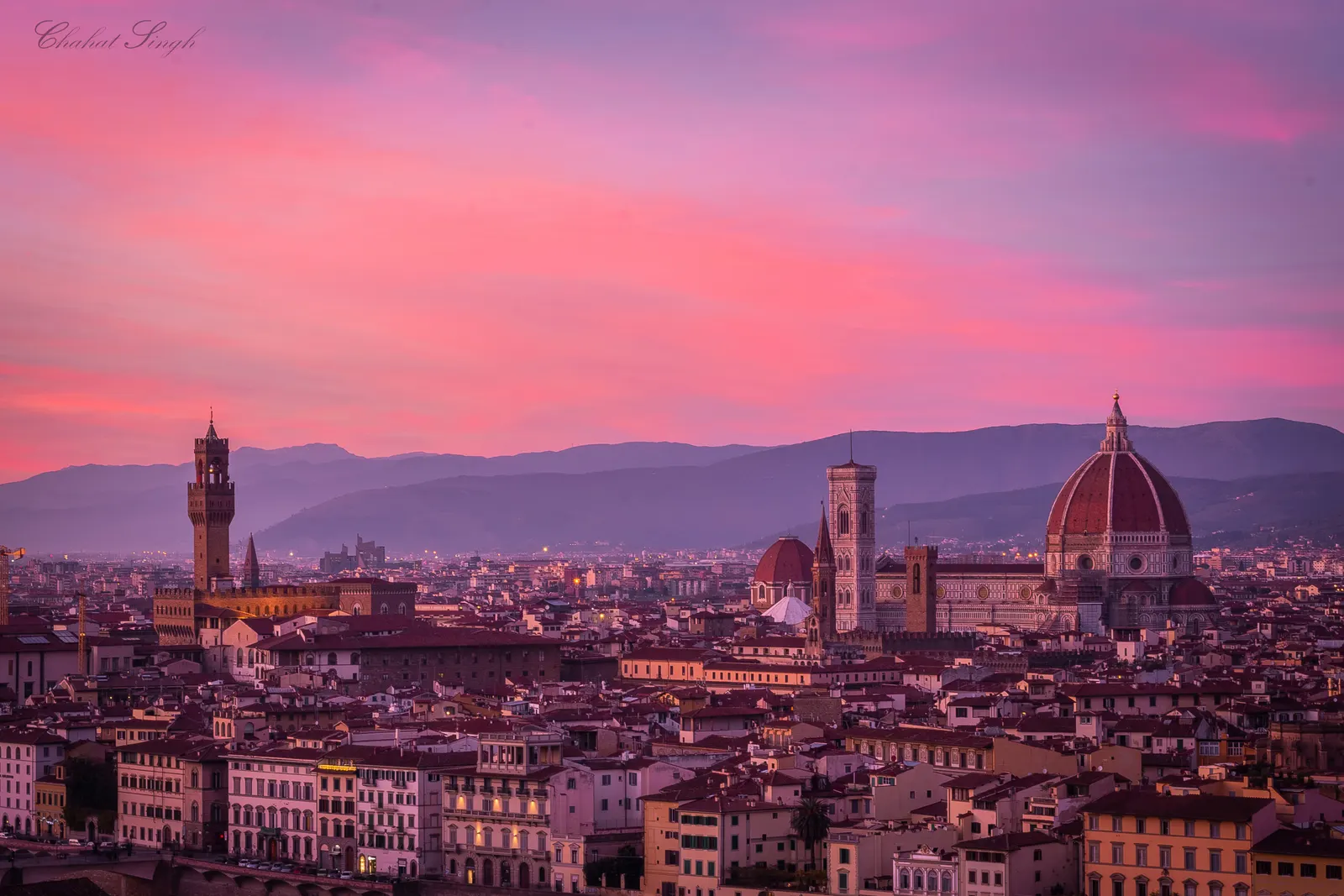 Florence's skyline at sunset, the Duomo's dome and bell tower rising above terracotta rooftops under a pink sky.