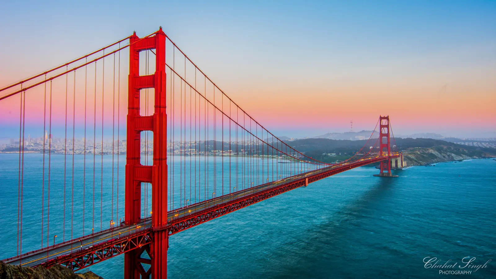 The Golden Gate Bridge's red towers spanning the bay at sunset, San Francisco's skyline in the distance.