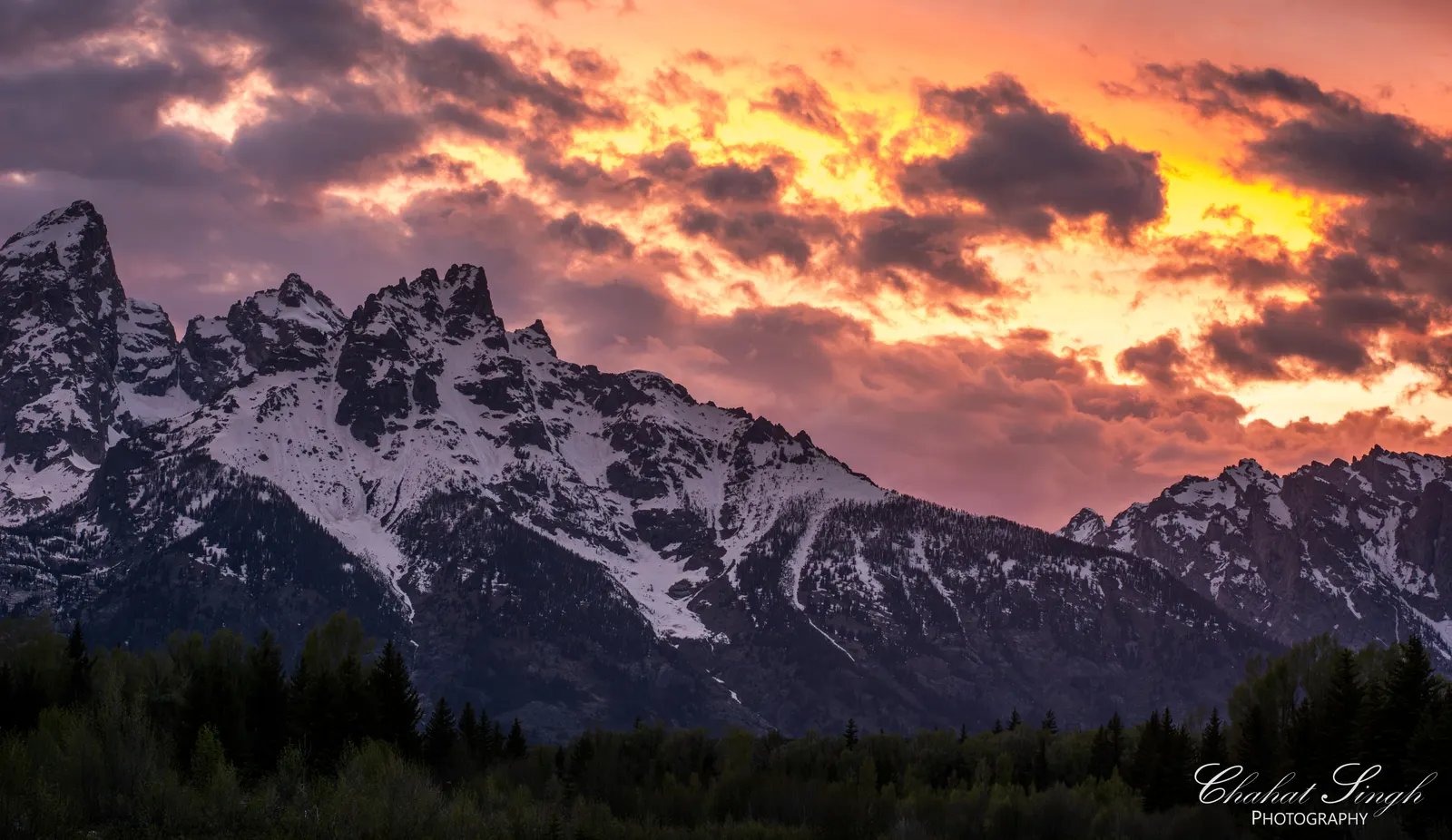 The Grand Teton mountain range silhouetted beneath a fiery orange and pink sunset sky.