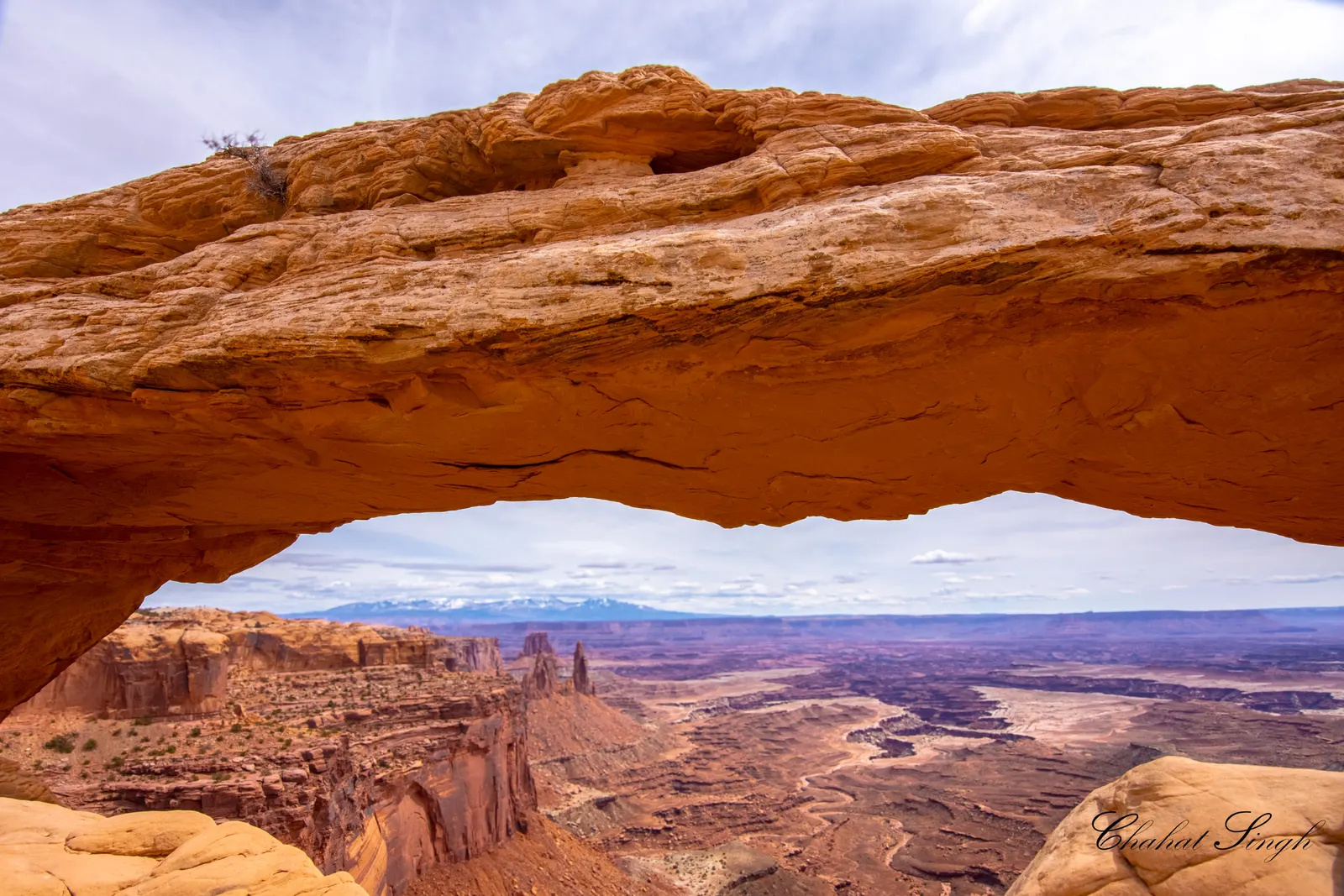 Mesa Arch framing a distant canyon view in Canyonlands National Park under a cloudy sky.