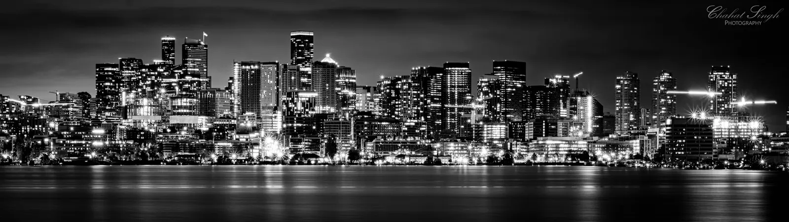 The Seattle skyline, including the Space Needle, lit up at night in a black-and-white panorama.