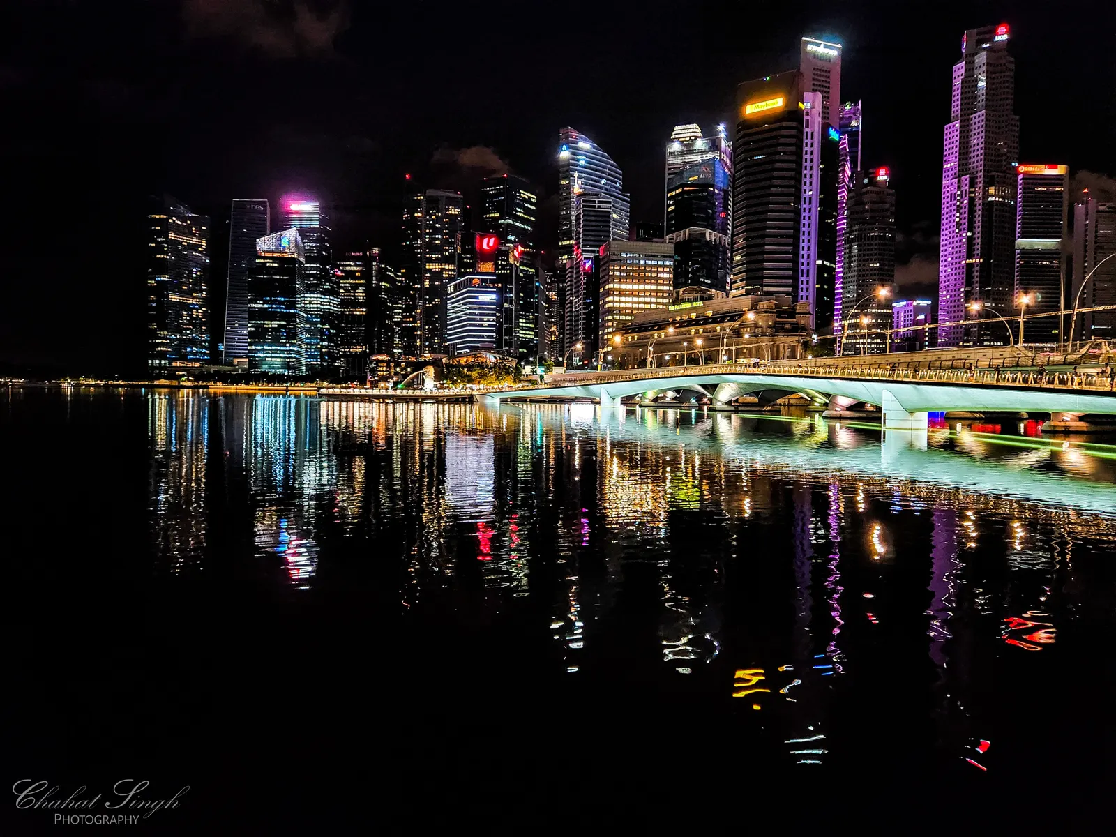Singapore's illuminated skyline and a lit bridge reflected in the water at night.