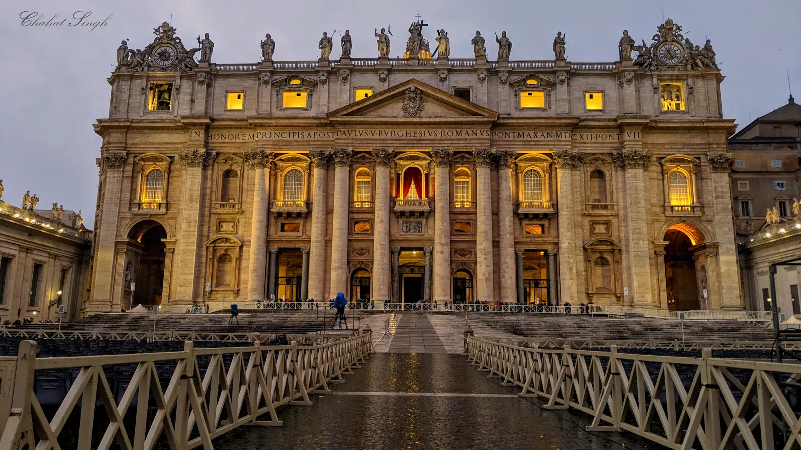 St. Peter's Basilica facade lit up in the evening, an empty square in front.
